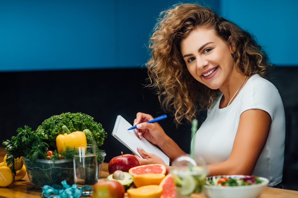 jeune femme assise à une table remplie de légumes et de fruits planifiant ses repas pour le régime pegan