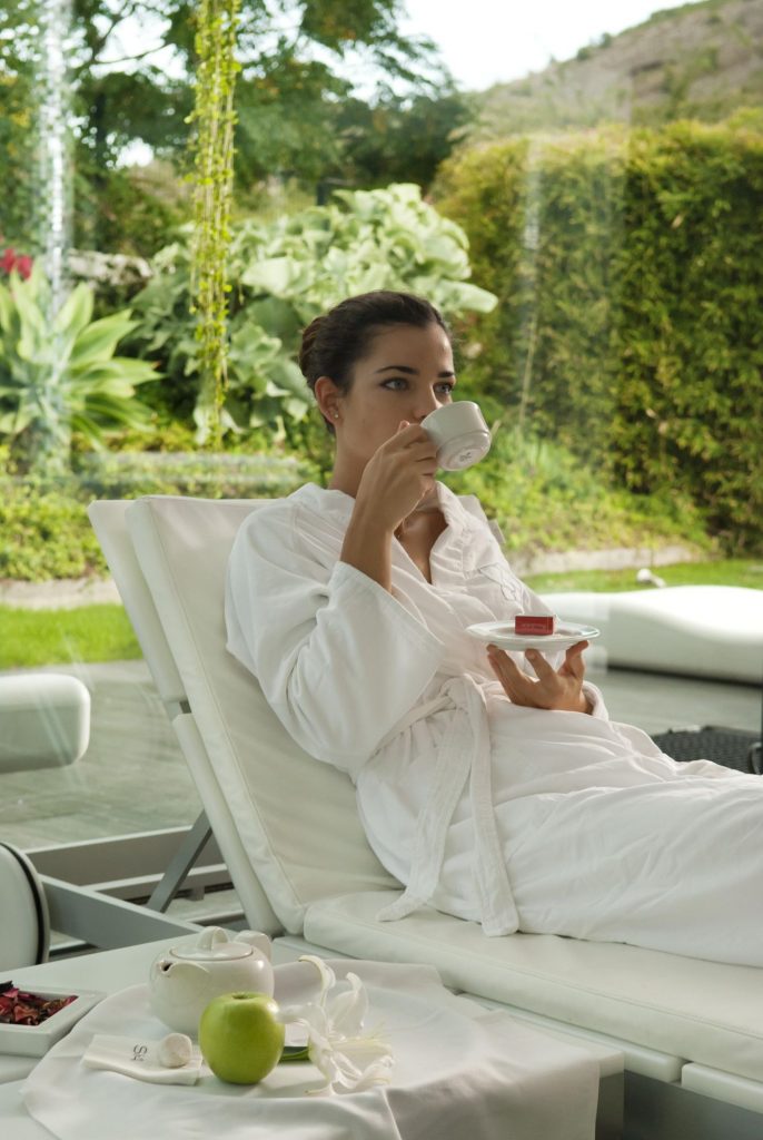 Une femme en peignoir blanc savoure une tasse de thé à l#hôtel Sha Wellness Clinic