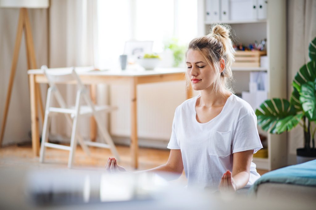 Une jeune femme fait des exercices de yoga à l'intérieur, chez elle, en méditant