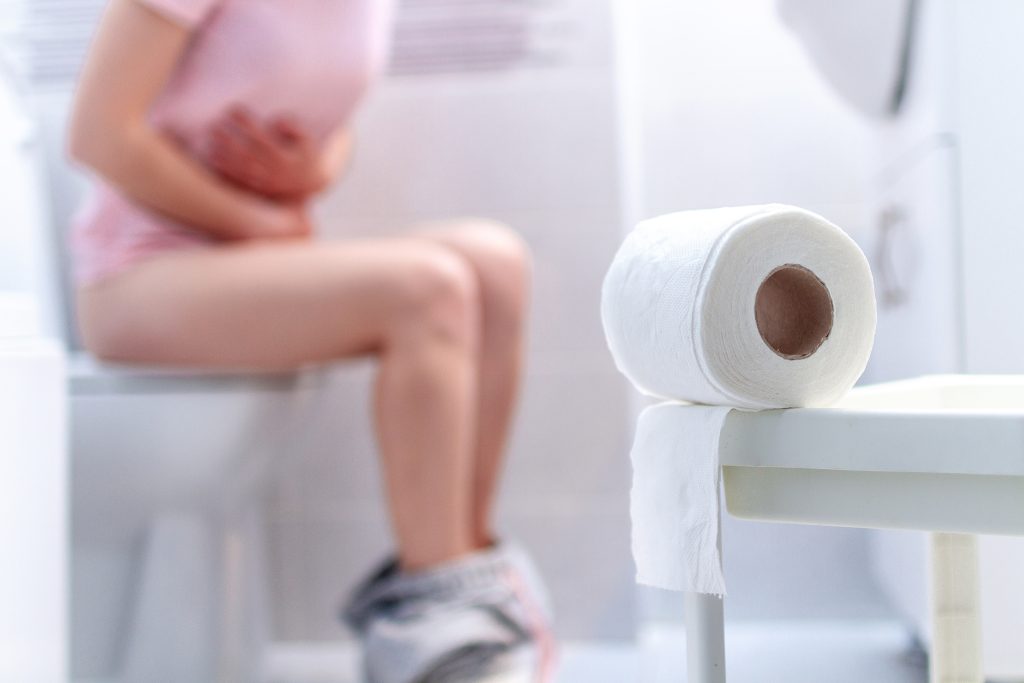 femme constipée sur les toilettes en arrière-plan, papier toilette en premier plan