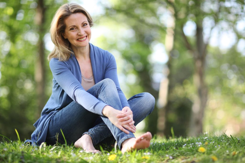 femme assise dans l'herbe et souriante se tenant la jambe