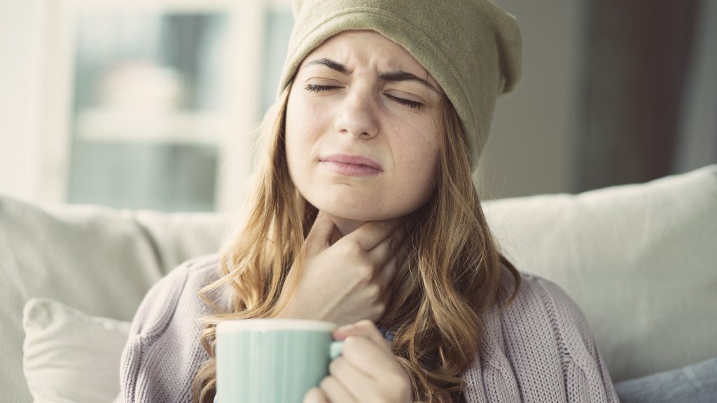 Ayurveda et mal de gorge, une femme se tient la gorge avec une main à cause de douleur à la gorge et boit une boisson chaude