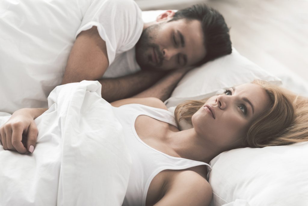 L'Ayurveda contre les troubles du sommeil, un couple allongé dans un lit l'homme dort et la femme n'arrive pas à dormir