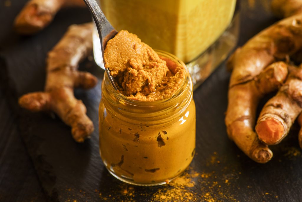 Ayurveda contre le rhume, pâte de curcuma dans un pot en verre avec une cuillère et du curcuma en arrière-plan